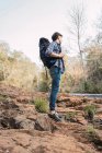 Randonneur masculin avec sac à dos debout sur un terrain rocheux près d'une cascade dans les bois et regardant loin — Photo de stock