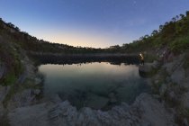 Viajante anônimo com tocha contemplando lagoa entre montanhas sob céu estrelado ao pôr do sol na Espanha — Fotografia de Stock