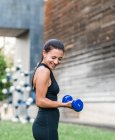 Atleta feminina determinada fazendo exercício com halteres durante o treino de fitness na rua da cidade no verão — Fotografia de Stock
