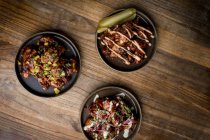 Set de deliciosas alitas de pollo a la parrilla en salsa BBQ servidas con verduras en platos redondos y colocadas sobre mesa de madera en restaurante - foto de stock