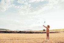 Side view of curly haired child standing in dry meadow and playing with toy windmill in summer — Stock Photo
