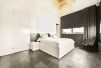 Просторная светлая спальня с двуспальной кроватью и ванной комнатой в современном мансардном стиле с белыми стенами и мраморным полом — стоковое фото
