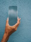 Ernte unkenntlich männlich zeigt moderne Handy mit schwarzem Bildschirm auf blauem Hintergrund in der Stadt — Stockfoto