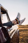 Side view of crop female chilling in vintage car with legs sticking out of window in evening in nature — Stock Photo
