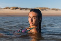 Ніжна жінка з мокрим волоссям плаває в спокійному морі в літній вечір і дивиться на камеру — стокове фото