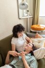 Tenera donna lesbica sdraiata sulle ginocchia della fidanzata amorevole seduta sul divano a casa e rilassante durante il fine settimana — Foto stock
