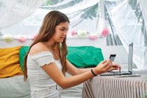 Mulher encantada sentada à mesa com laptop e fazendo compra com cartão de plástico durante compras on-line na tenda do quintal — Fotografia de Stock