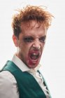 Эксцентричный мужской актер с размазанным макияжем, кричащий от злости во время выступления на белом фоне — стоковое фото