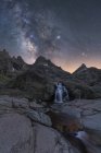 Захватывающий вид высоких грубых гор с каскадом и рекой под звездным небом с галактикой в вечернее время — стоковое фото