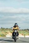 Focused female bike in helmet riding modern motorbike along road on sunny day and looking at camera — Stock Photo