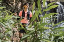 Viaggiatore maschile con bastoncini da trekking a piedi lungo sentiero vicino alla cascata nella foresta tropicale — Foto stock