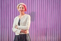 Charming alternative female with dyed hair and in trendy clothes standing against violet wall in city and looking away — Stock Photo