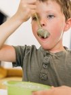 Adorable garçon mangeant une soupe à la crème appétissante avec une cuillère pendant le déjeuner à la maison — Photo de stock
