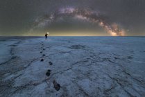 Silhouette of explorer standing in dry salt lagoon holding a flashlight on background of starry sky with glowing Milky Way at night — Stock Photo