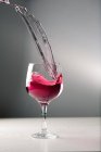 Kaltes alkoholrotes Getränk spritzt im Atelier aus Glaskelch auf grauem Hintergrund — Stockfoto