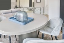 Elegante diseño interior del hogar con cómodas sillas suaves colocadas alrededor de una mesa ovalada con jarrón decorativo en la sala de estar moderna - foto de stock