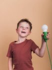 Обдумывание ребенка в футболке с пластиковой лампочкой представляет идею концепции глядя на бежевый фон — стоковое фото