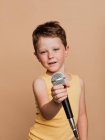 Criança legal em cantar no microfone moderno em fundo marrom no estúdio — Fotografia de Stock