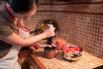Femme au foyer anonyme mélangeant des tomates dans un mélangeur tout en préparant la sauce marinara dans la cuisine à la maison — Photo de stock