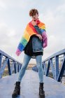From below of serious homosexual male standing with rainbow flag on bridge and looking at camera — Stock Photo
