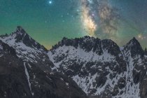 Vista espetacular da galáxia no céu com gás interestelar sobre o monte majestoso áspero com neve à noite — Fotografia de Stock