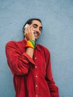 Delighted ethnic gay male with rainbow bandana on hand speaking on cellphone while standing near gray wall in city and looking at camera — Stock Photo
