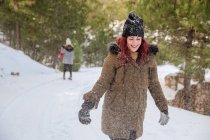 Веселая женщина в верхней одежде, стоящая в зимнем лесу и выбрасывающая снег, веселясь — стоковое фото
