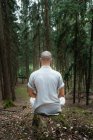 Вид ззаду на невпізнаваного чоловіка в традиційному одязі, що сидить на скелі в позі Лотоса і медитує під час тренування кунг-фу в лісі — стокове фото