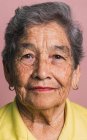 Пожилая женщина с короткими седыми волосами и карими глазами смотрит на камеру на розовом фоне в студии — стоковое фото