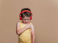 Задоволений хлопчик у червоних навушниках слухає музику на коричневому фоні в студії — стокове фото