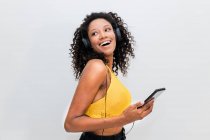 Щаслива афроамериканська жінка в навушниках з мобільним танцем, слухаючи пісню на світлому фоні — стокове фото