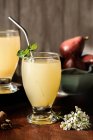 Vasos de deliciosas bebidas refrescantes con jugo de pera y hojas frescas de saúco en la mesa con palitos de canela - foto de stock