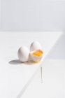 Ângulo alto de ovo inteiro e quebrado com gema de ovo com casca colocada na borda da mesa no fundo branco no estúdio — Fotografia de Stock