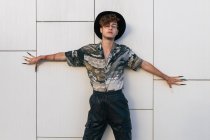 Young vain man in stylish wear with hat standing on tiled wall looking away — Stock Photo