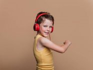 Satisfait garçon préadolescent dans des écouteurs rouges écoutant de la musique sur fond brun en studio — Photo de stock