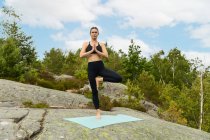 Full body barefoot female doing Tree pose on mat while practicing yoga on stone in nature — Stock Photo