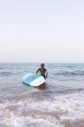Rückenansicht einer nicht wiedererkennbaren Frau im Badeanzug, die im Sommer mit SUP-Board im Meerwasser steht — Stockfoto