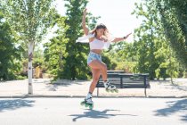 Vista lateral do ajuste fêmea em patins mostrando acrobacias na estrada na cidade no verão — Fotografia de Stock
