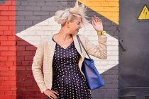 Carefree alternative female throwing dyed short hair against colorful wall in urban area — Stock Photo