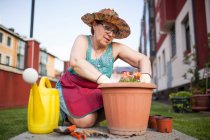 Знизу зріла жінка садівник переносить рослину до великого вазона в її домашньому саду — стокове фото