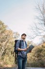 Низкий угол мужчины туриста с рюкзаком навигации с бумажной картой, стоя в лесу и глядя в сторону — стоковое фото