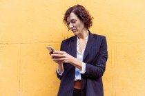 Самоуверенная элегантная женщина в формальной одежде стоит и смотрит на экран мобильного телефона — стоковое фото