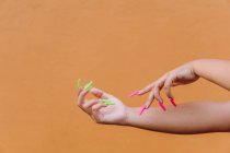 Crop femelle anonyme avec ongles longs manucurés toucher délicatement la peau de la main sur fond orange — Photo de stock