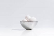 Миска зі свіжими курячими яйцями, розміщеними на столі на білому тлі в студії — стокове фото