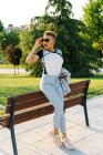 Trendy ethnic female in sunglasses with smartphone and modern haircut looking away on tiled pavement in town — Stock Photo