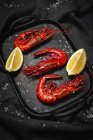Camarão vermelho cozido delicioso na bandeja com sal grosso e pedaços de limão suculentos no fundo escuro — Fotografia de Stock