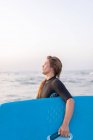 Vista lateral da fêmea em maiô de pé com placa SUP na água do mar no verão e olhando para longe — Fotografia de Stock