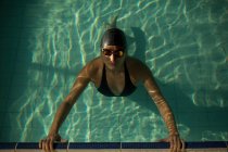Молодая красивая женщина на бордюре крытого бассейна, в черном купальнике, плавающая в воде — стоковое фото