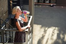 High angle side view of joyful alternative female with dyed hair and in braces standing on stairs with reusable cup of hot takeaway drink and looking at camera — Stock Photo