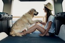 Barfüßige Frau hält Pfote des treuen Golden Retriever-Hundes, während sie im Wohnmobil auf dem Bett sitzt, während sie in der Natur unterwegs ist — Stockfoto
